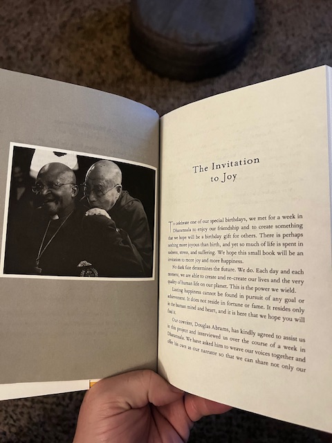 Image of The Book of Joy open to "The Invitation to Joy" on the right, with picture of Desmond Tutu and the Dalai Lama on the left. 