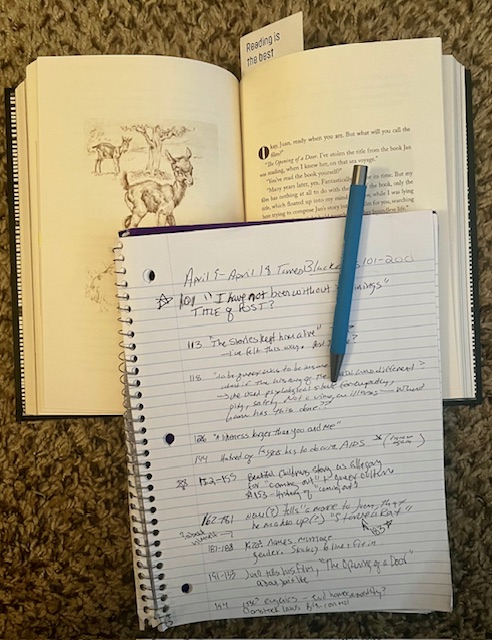 Picture of note book, filled with reading notes, with blue pen attached and sitting atop open book, with bookmark. 