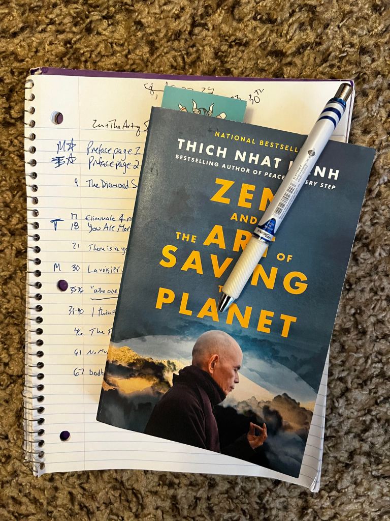 Paperback copy of Zen and the Art of Saving the Planet sitting atop spiral notebook with notes in blue ink, blue pen clipped to book's cover.